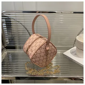 Detail of pink cylindrical mini bag with M-pattern print and golden metal chain strap