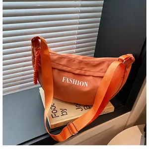 Detail of orange nylon dumpling bag featuring white fashion print and woven zipper pull