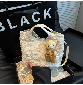 Detailed shot of cream pleated bucket bag with plush bear charm and leather strap