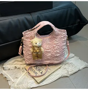 Detail of pink pleated bucket bag with plush bear charm and crossbody strap
