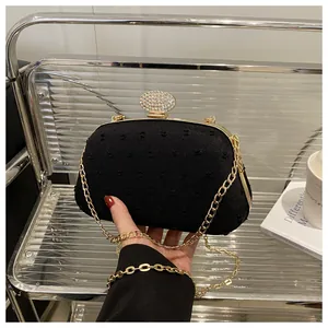 Detailed view of the black textured evening bag with gold chain and crystal clasp