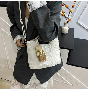 Detail of white pleated bucket bag with a cute bear pendant and a smooth shoulder strap