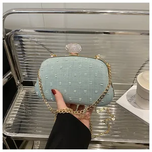 Close-up of light blue textured evening clutch with crystal clasp and gold chain strap