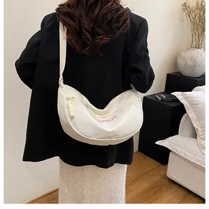 Detail of a beige crescent crossbody bag with FASHION logo and knot zipper on a model