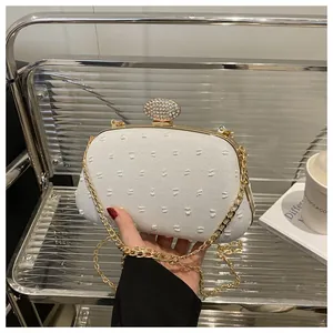 Detail of white jacquard fabric clutch with luxury gold rhinestone clasp and chain strap