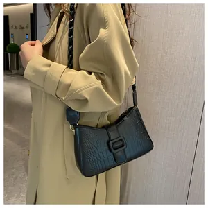 Detail of black crocodile pattern faux leather shoulder bag with wide strap on trench coat