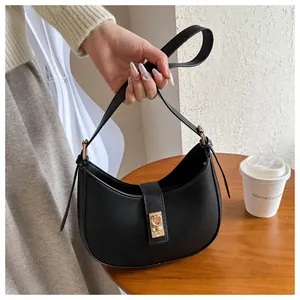 Detail of minimalist black crescent bag with gold buckle on wooden cafe table
