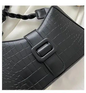 Detail of black crocodile pattern faux leather bag with woven strap and square buckle