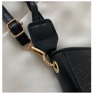 Detail of gold metal hook and buckle on black crocodile pattern leather shoulder bag