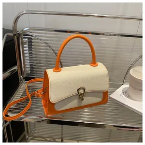Detail of orange and white canvas tote bag with gold metal clasp on a glass shelf