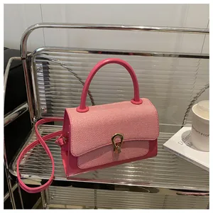 Pink crossbody bag with woven texture flap and gold horseshoe lock detail on glass shelf