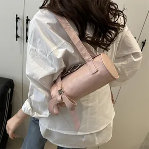 Pink cylinder shoulder bag with bow ribbon detail shown on model in minimalist style