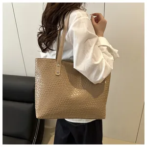 Model wearing a large khaki textured leather tote bag with silver rivets details