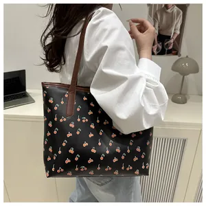 Détail d'un sac cabas noir avec motifs cerises et lanières marron sur un mannequin