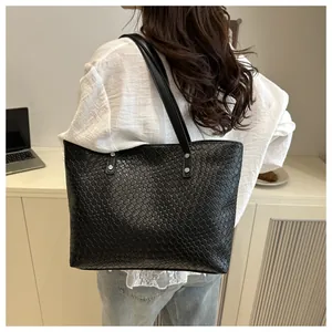 Detail of a large black woven tote bag with silver rivets and leather straps for women