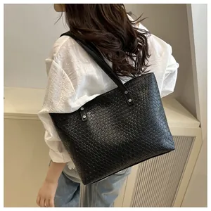 Detail of black woven tote bag with silver rivets shown on shoulder for size context