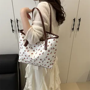 Sac fourre-tout à imprimé cerise avec anses en cuir marron porté par une femme en robe
