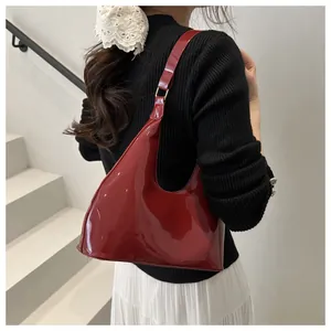 Detail van bordeauxrode laklederen hobo tas met gouden gesp op de schouder van model