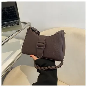 Detail of dark brown crocodile-embossed handbag with woven handle and large decorative buckle