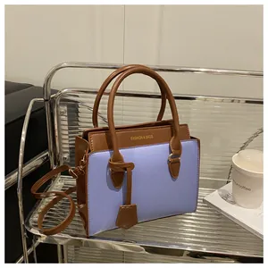 Detail of two-tone pebbled leather handbag with gold lettering on a modern display shelf