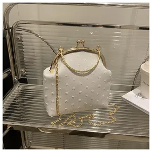 Dettaglio borsa in tessuto bianco con chiusura vintage dorata e tracolla a catena