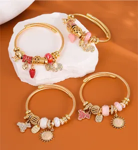 Detailed view of gold beaded bangles with strawberry, elephant and crown charms