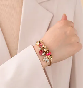 Detail of a gold charm bracelet with red strawberry and crystal elephant on a model
