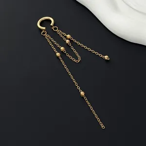 Detailed view of a gold tassel ear cuff with long chains on a black matte background