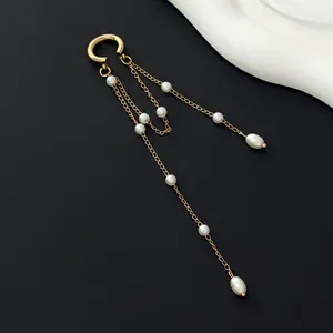 Close-up of elegant gold tassel ear cuff with hanging pearls on a dark background