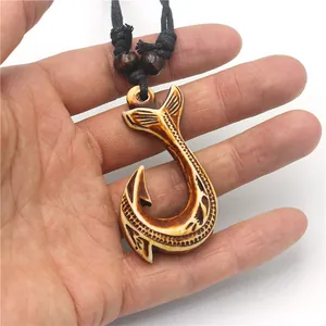 Close-up of Maori fish hook resin pendant with tribal carvings held in a hand