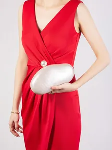 Iridescent white acrylic shell evening clutch bag held by model in a red formal dress