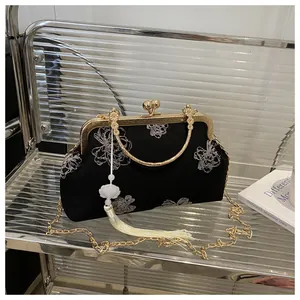 Close-up of black floral embroidery on retro shell bag with gold chain and tassel