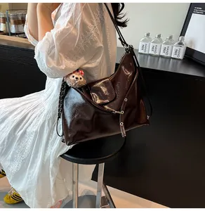 Detail of glossy brown patent leather hobo bag with adjustable strap and metal buckles