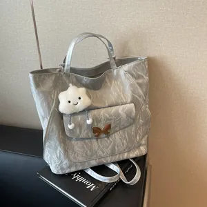 Silver tote bag with marble texture and cloud charm on a sofa with magazines