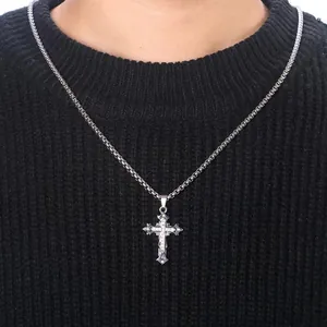 Detailed close-up of a silver cross pendant with embedded crystals on a black knit sweater