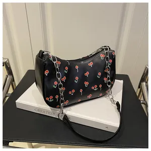 Detail of a black leather bag with red cherry print, silver chain and zipper closure
