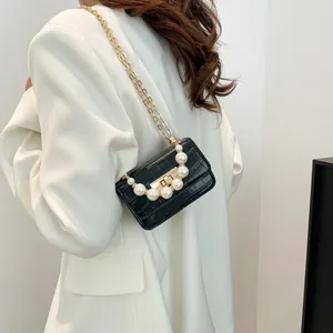 Fashionable black faux crocodile jelly bag with pearl handle and golden chain on white suit