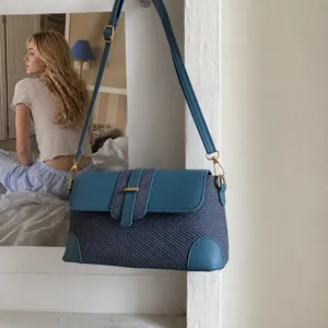 Sac baguette bleu en patchwork de tweed avec fermoir doré suspendu au mur blanc