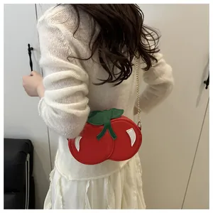Detailed view of red cherry-shaped shoulder bag with green leaves and gold chain strap