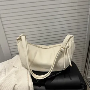 Minimalist beige crescent-shaped leather hobo bag with adjustable strap on pedestal