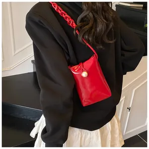 Macro detail of red glossy mini crossbody bag featuring a large white pearl buckle