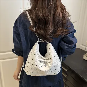 Borsa a secchiello bianca trapuntata a fiori neri con fiocco, indossata da modella