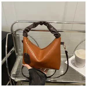 Detailed close-up of orange-brown pleated handbag with coffee-colored cloud handle