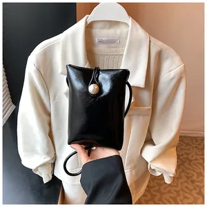 Detail of a mini black glossy shoulder bag featuring a large pearl button and fine leather texture