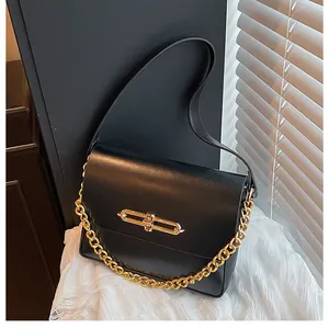 Close-up of minimalist black leather handbag with gold metal lock and chunky chain detail