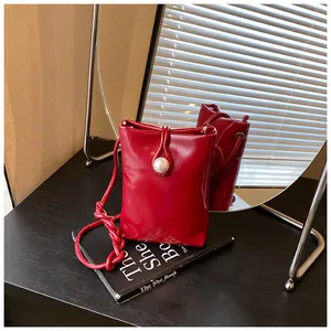 Detail of red glossy mini bag with a large pearl buckle and knotted braided strap