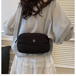 Detail of minimalist black nylon crossbody bag with silver M logo on a female model