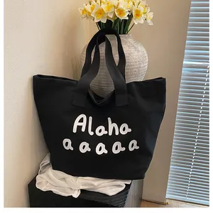 Détail du sac cabas en toile noire montrant le lettrage blanc et un grand compartiment