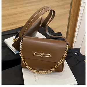 Detail of a brown leather crossbody bag featuring a sleek gold bar clasp and chunky chain