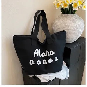 Gros plan d'un cabas en toile noire avec lettrage Alaha sur une table en bois